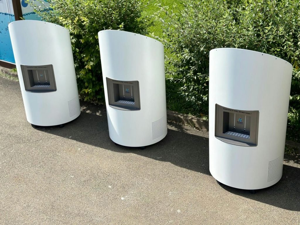 Trois fontaines à eau Cascatell'O blanches et modernes sont placés sur une surface pavée, disposés en rangée de gauche à droite.