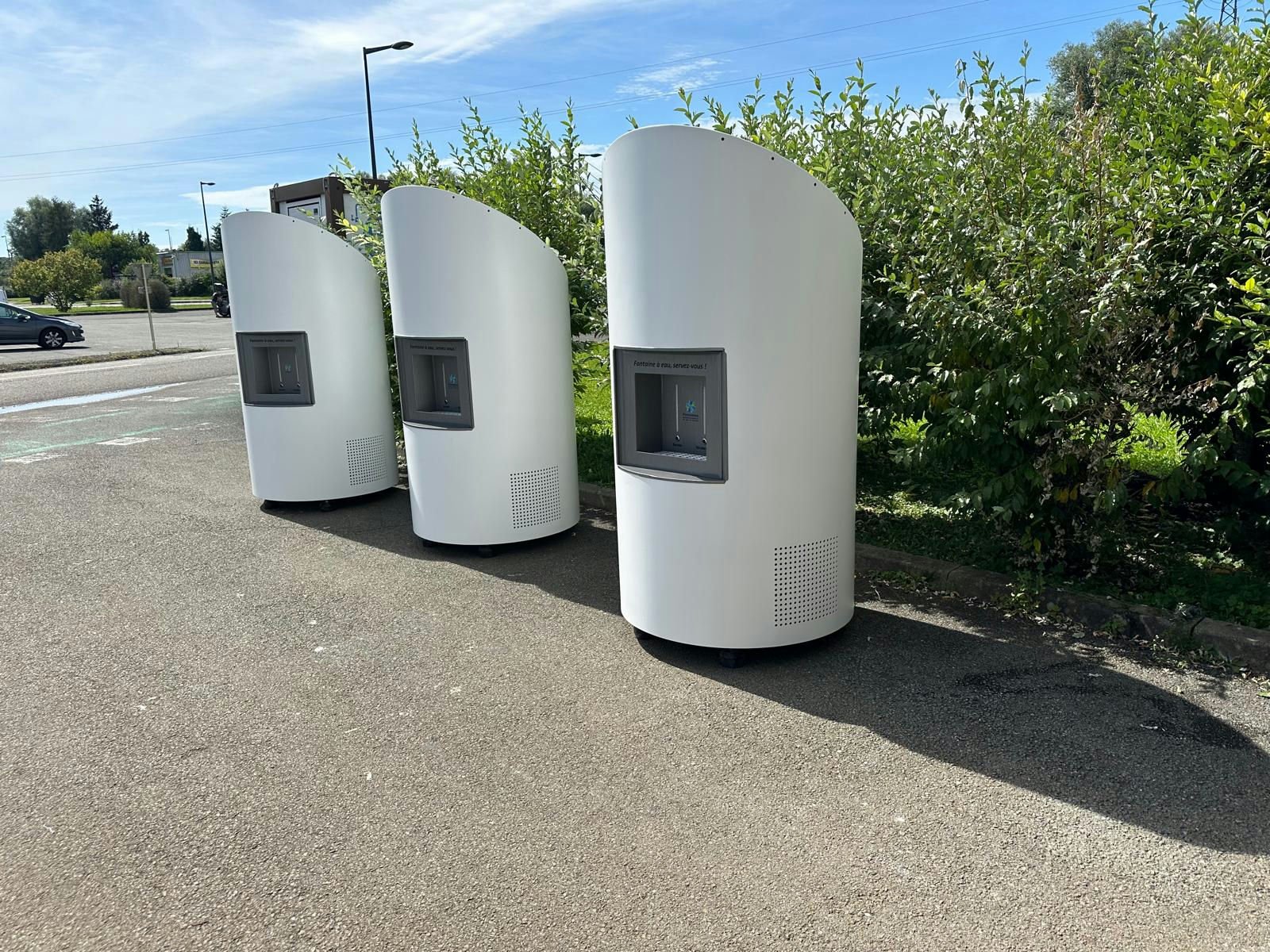 Trois fontaines à eau Cascatell'O blanches et modernes sont placés sur une surface pavée, disposés en rangée de gauche à droite.