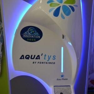 Fontaine à eau blanche avec un logo de Fontaineo et les mots « Aqua'tys by Fontaineo » et « Innovation 2025 ». La fontaine est dotée d'une fente étiquetée « Eau Plate » avec une grille circulaire en dessous, entourée d'un éclairage bleu.