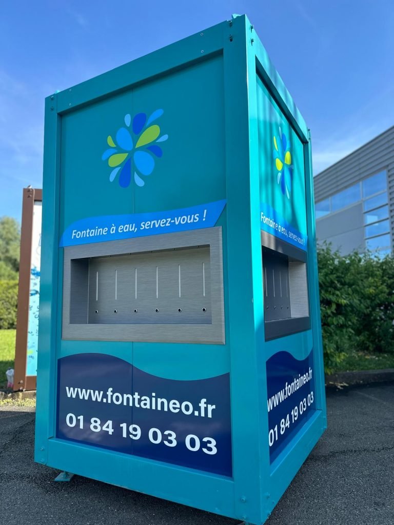 Un distributeur d'eau bleu sarcelle est présenté à l'extérieur, avec des logos représentant des gouttes d'eau bleues et vertes. Il est écrit « Fontaine à eau, servez-vous ! » et affiche un site Web et un numéro de téléphone. Un bâtiment et de la verdure sont visibles en arrière-plan.