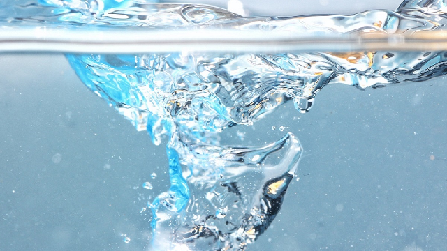 Une eau claire avec des bulles d'air et des éclaboussures est photographiée sous l'eau. L'image capture le mouvement et la fluidité de l'eau sur un fond bleu clair.