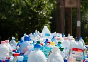Une grande collection de bouteilles en plastique, principalement des bouteilles d'eau et de boissons, sont regroupées à l'extérieur avec de la verdure et des arbres flous à l'arrière-plan.