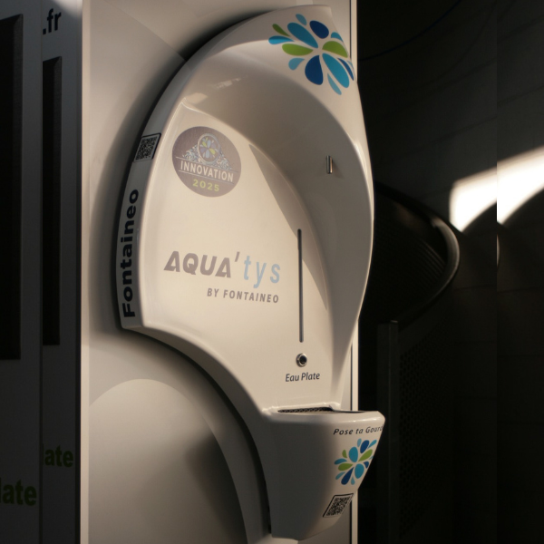 Une fontaine à eau blanche de la marque « Fontaineo » et du modèle « AQUA’tYs » est présentée. Elle est équipée d’un distributeur circulaire portant le logo « Eau Plate » et un autocollant de récompense intitulé « Innovation 2025 ».