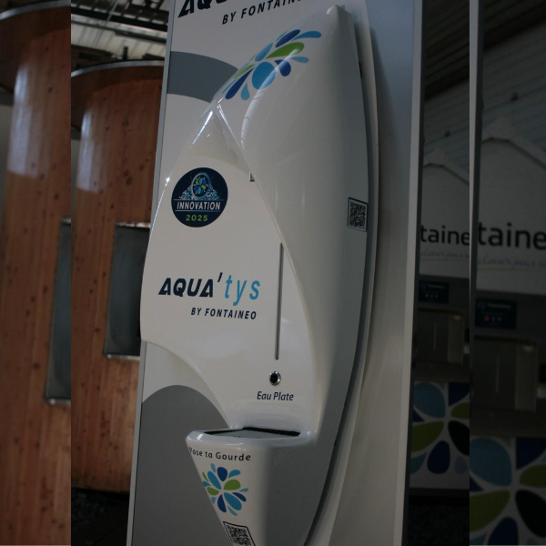 Fontaine à eau « AQUA'tys by Fontaigue » au design incurvé. Elle arbore le logo « Innovation 2025 ». Elle est destinée à l'« Eau Plate » (eau plate) et dispose d'une fente pour « Rase la Gourde ».