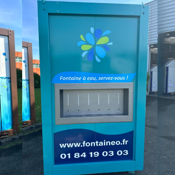 Fontaine à eau bleue et turquoise ornée d'un motif floral en haut. L'inscription « Fontaine à eau, servez-vous ! » est accompagnée de l'adresse du site web et d'un numéro de téléphone en bas. La machine est équipée de plusieurs buses de distribution. Un bâtiment est visible en arrière-plan.