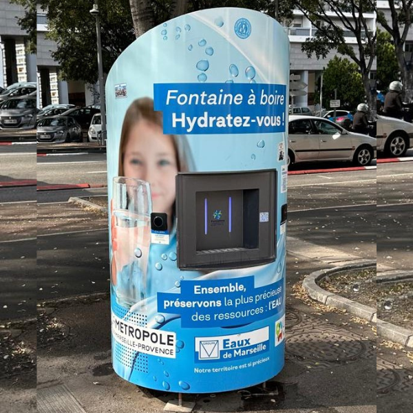 Une fontaine d'eau publique à l'extérieur bleu présente le graphisme d'une personne tenant un verre d'eau. Le texte sur la fontaine dit : « Fontaine à boire, Hydratez-vous ! » et « Ensemble, préservons la plus précieuse des ressources : l'EAU.
