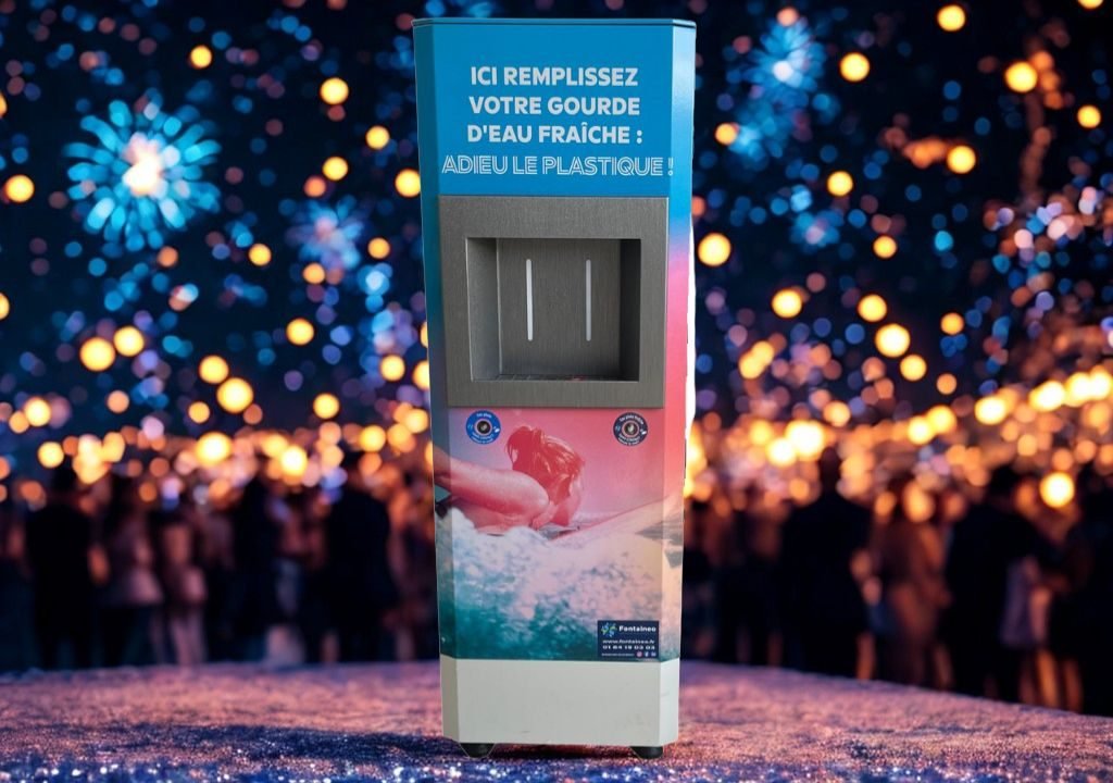 Una estación de llenado de agua con texto en francés se alza de noche frente a una multitud borrosa, con muchas luces brillantes y un ambiente festivo de fondo.