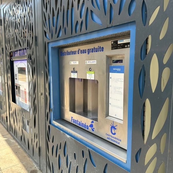 Un distributeur d'eau gratuit et public, étiqueté "Fontainéo", est encastré dans un mur métallique à motifs. Au-dessus des robinets, des instructions et des options pour de l'eau plate ou de l'eau gazeuse sont affichées. Le logo de Châteauroux Métropole est visible.